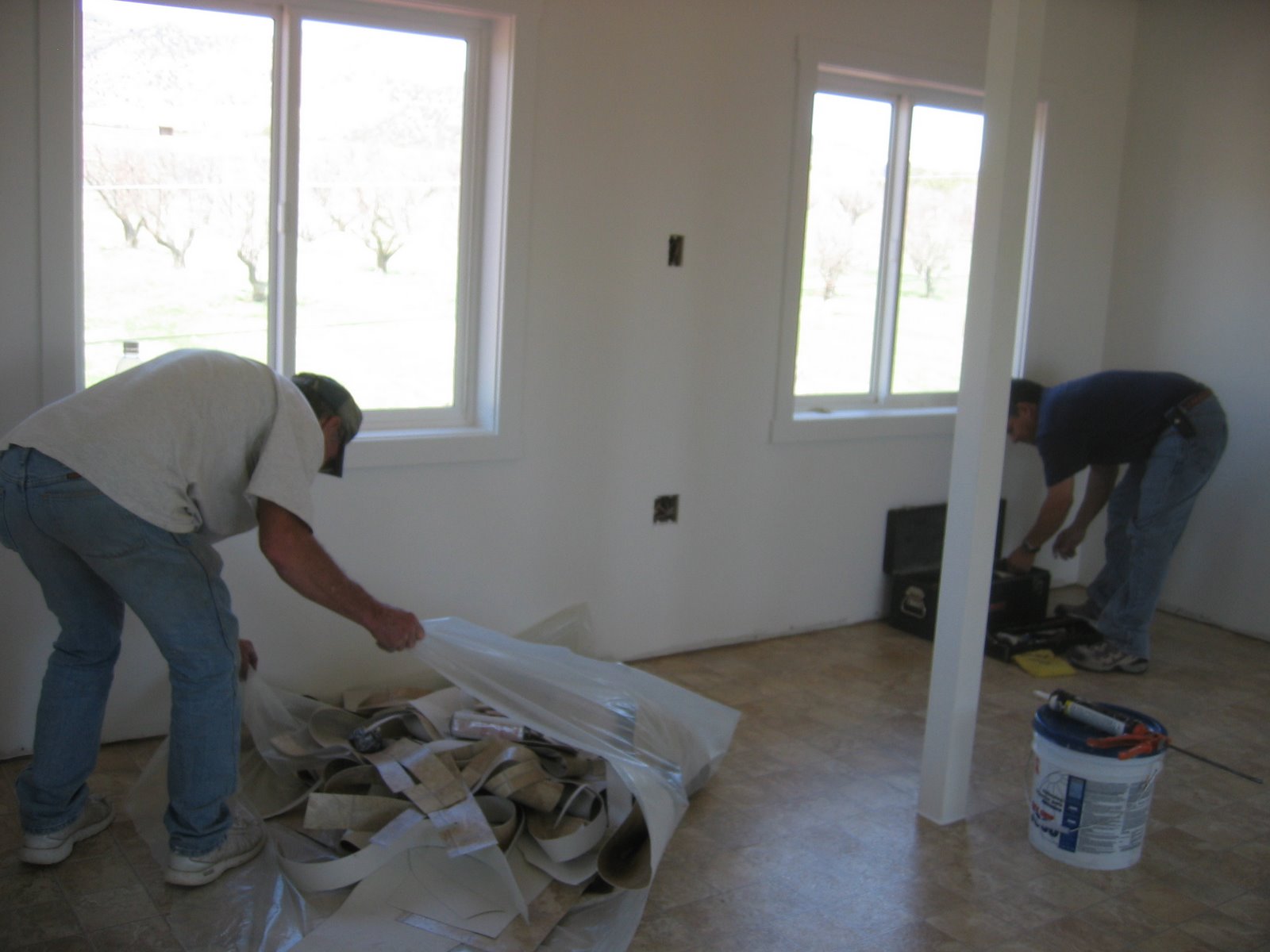 Two construction men work on cleaning up their supplies after installing the linoleum floor. 