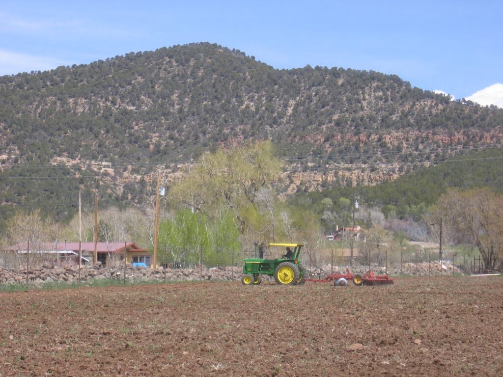 A tractor is driving through this field, getting it ready for planting fresh pasture. 