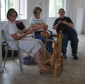 Margaret, Monica, and Elena sit together next to a spinning wheel.