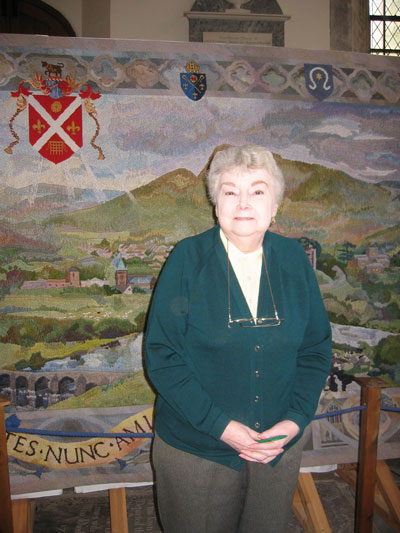 A woman who contributed to the tapestry poses in front of it.