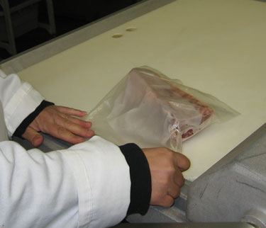 This worker is preparing to vacuum seal a cut of meat.
