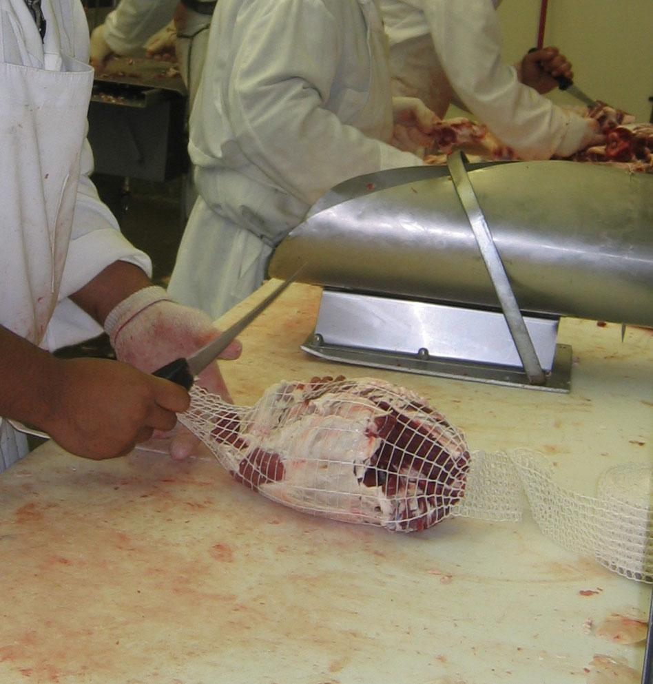 This worker is purring a boneless leg roast into a mesh bag for cooking.
