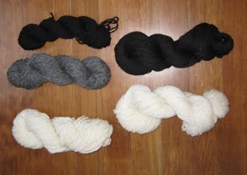 An assortment of black, white, and grey yarns are laid out for viewing on a wood floor. 