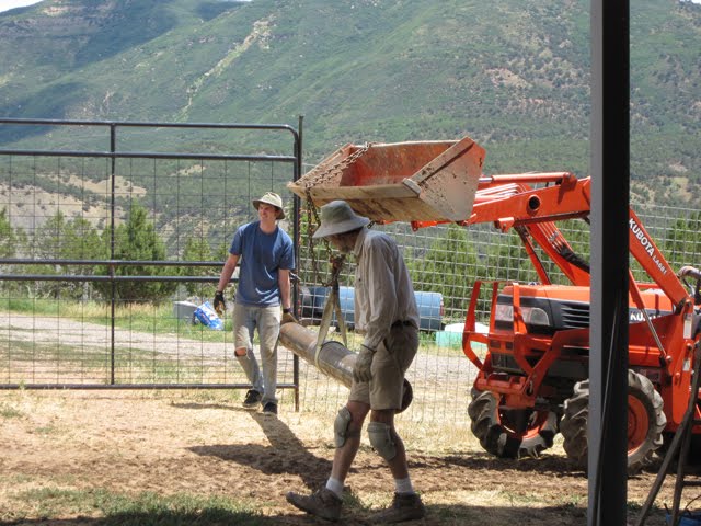 A crew of men uses an orange tractor to move a large metal pole.