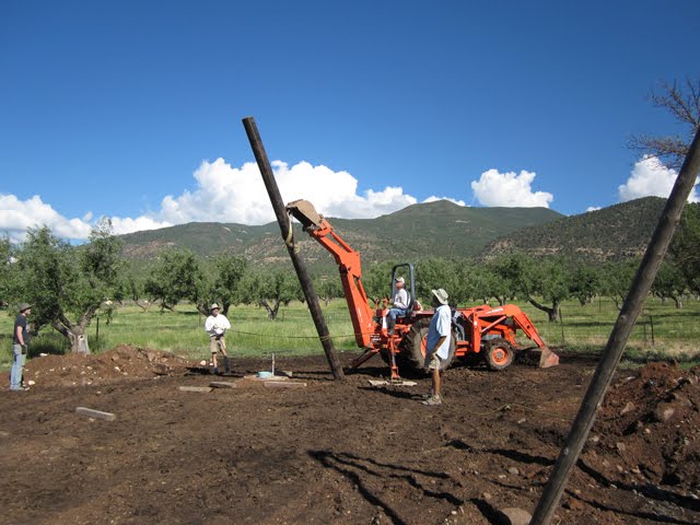 A tractor with a backhoe attachment is used to right the poles.