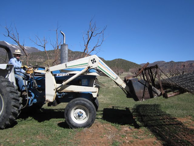 A man drives a white tractor with a brush rake attached to the bucket.
