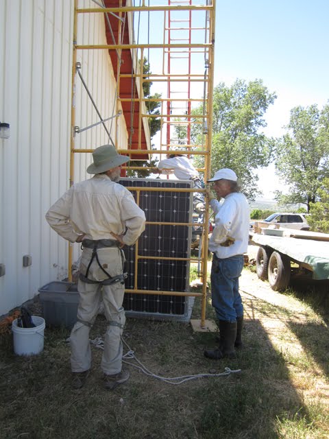 Several men stand around some scaffolding, getting ready to hoist a solar panel up onto a roof. 