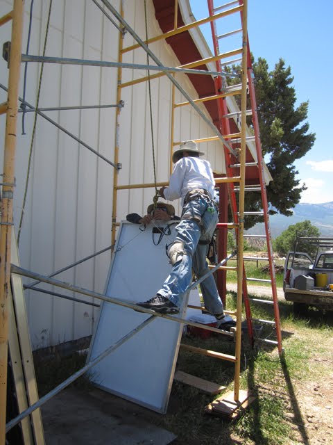 Two workers strap a solar panel into a pulley system. 