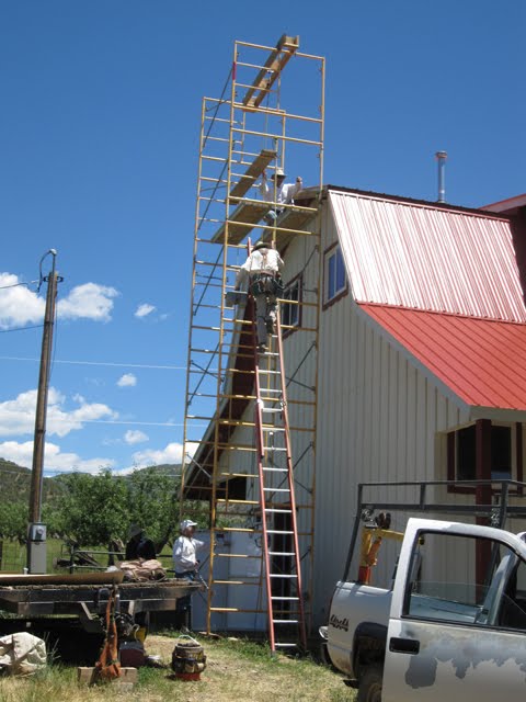 Three men work around incredibly tall scaffolding next to the shop. 