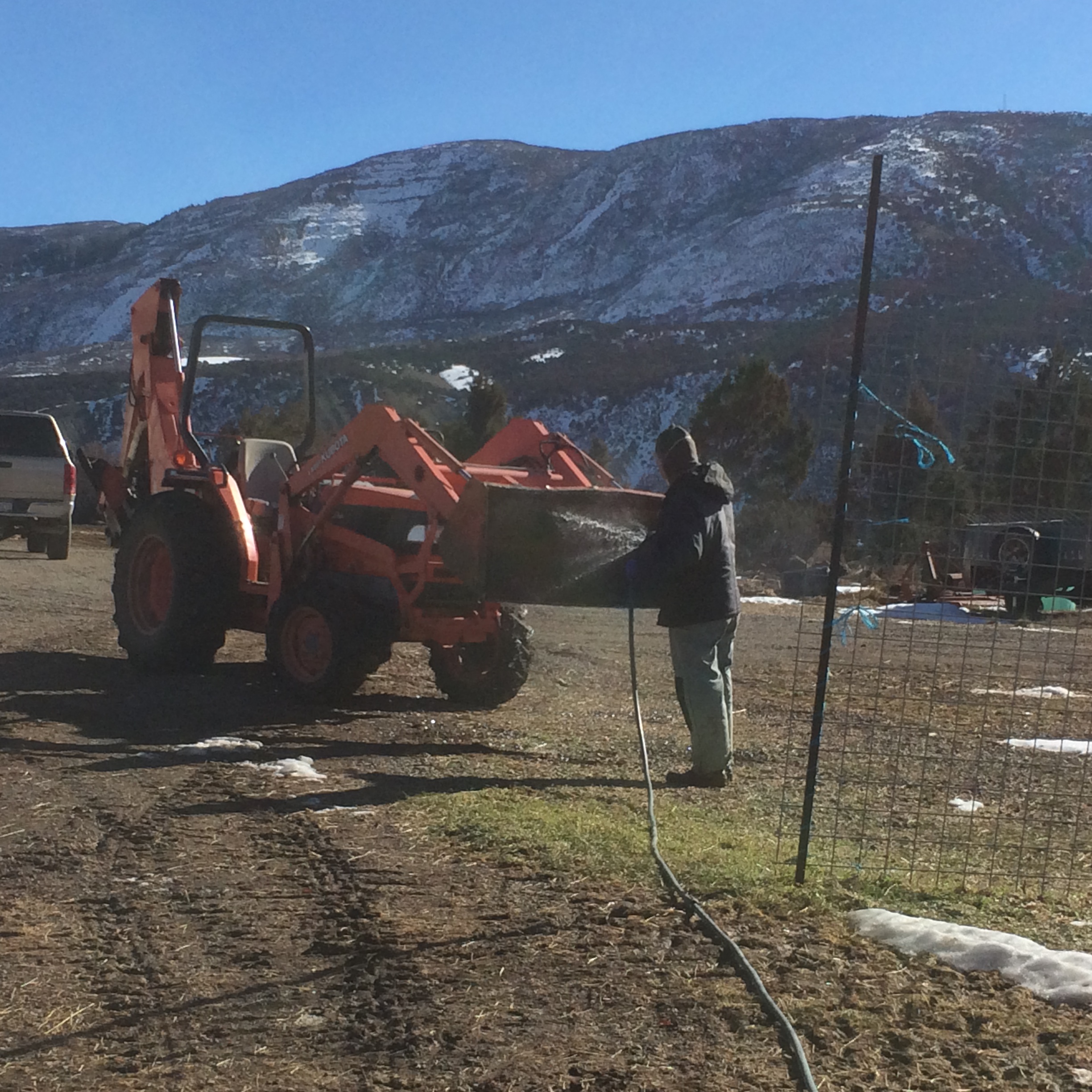 Ken uses a hose to watch out the bucket of an orange tractor. 