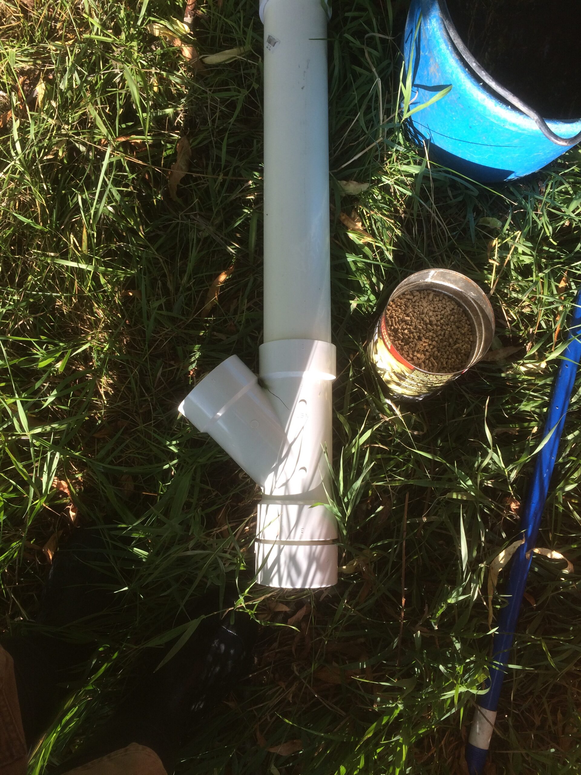 Another view of the PVC chicken feeder laying in the grass. 