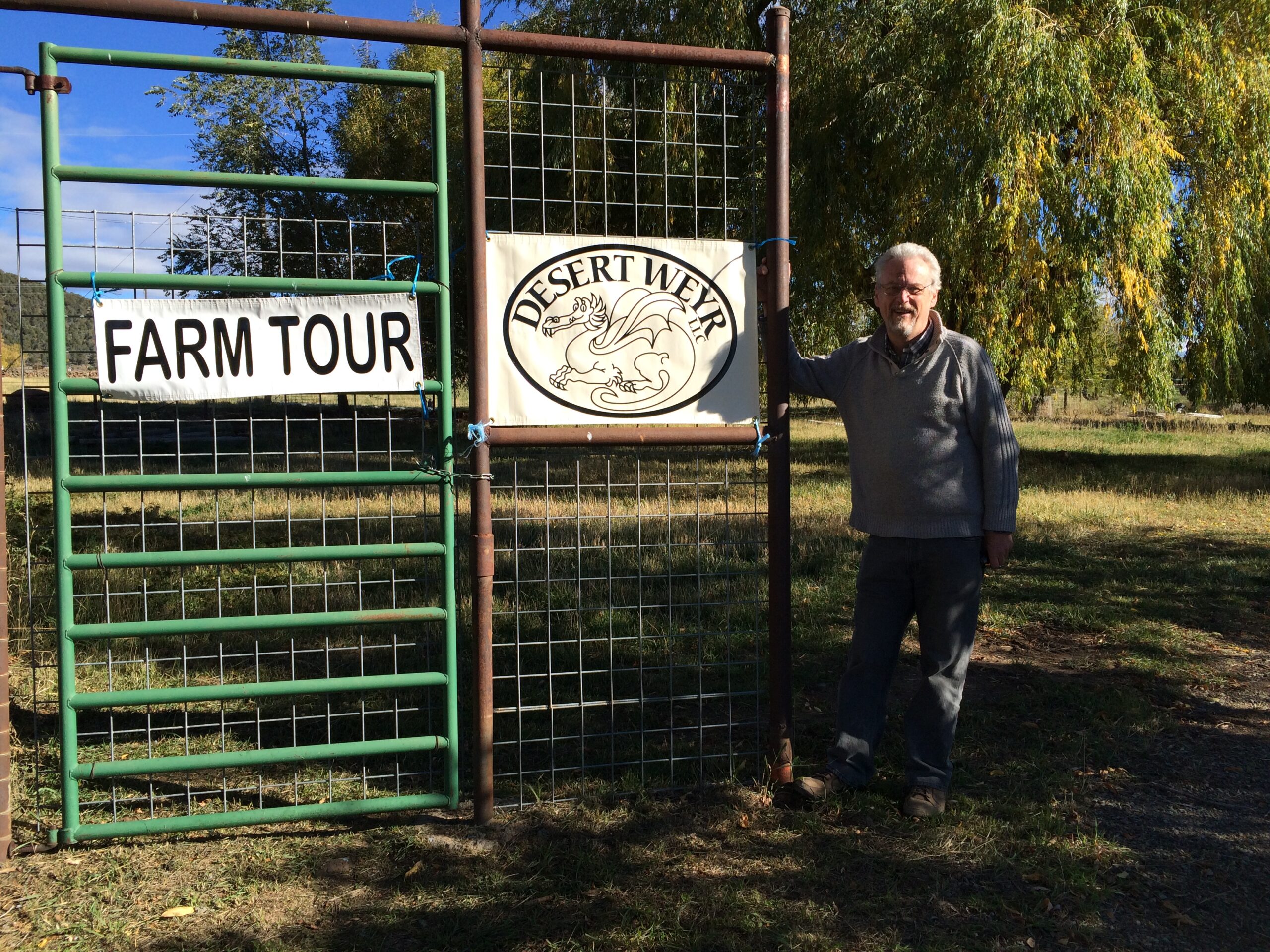 A man stands next to the Desert Weyr, LLC farm sign. 