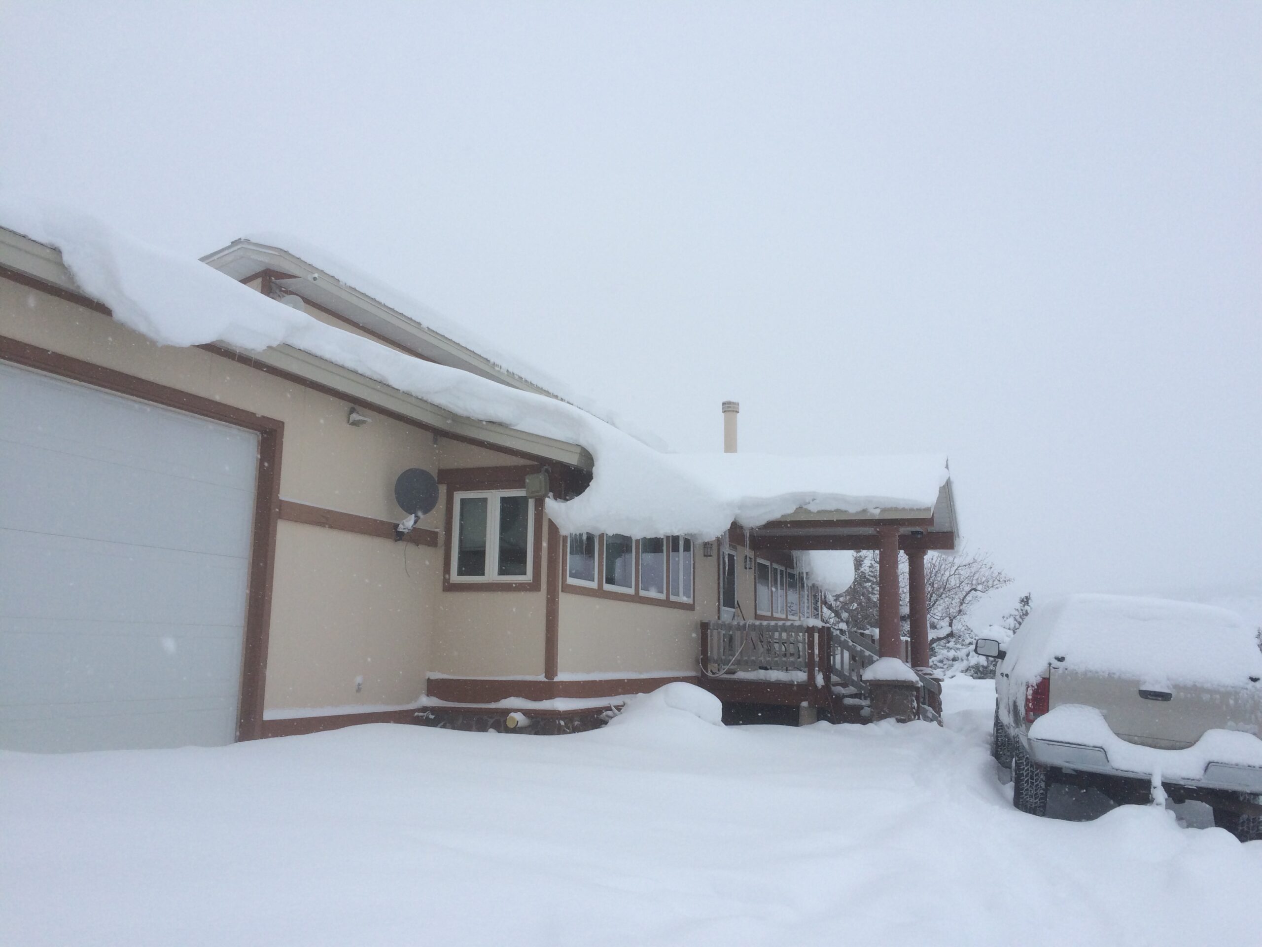 An attached garage, porch, and vehicle are draped in heavy snow.
