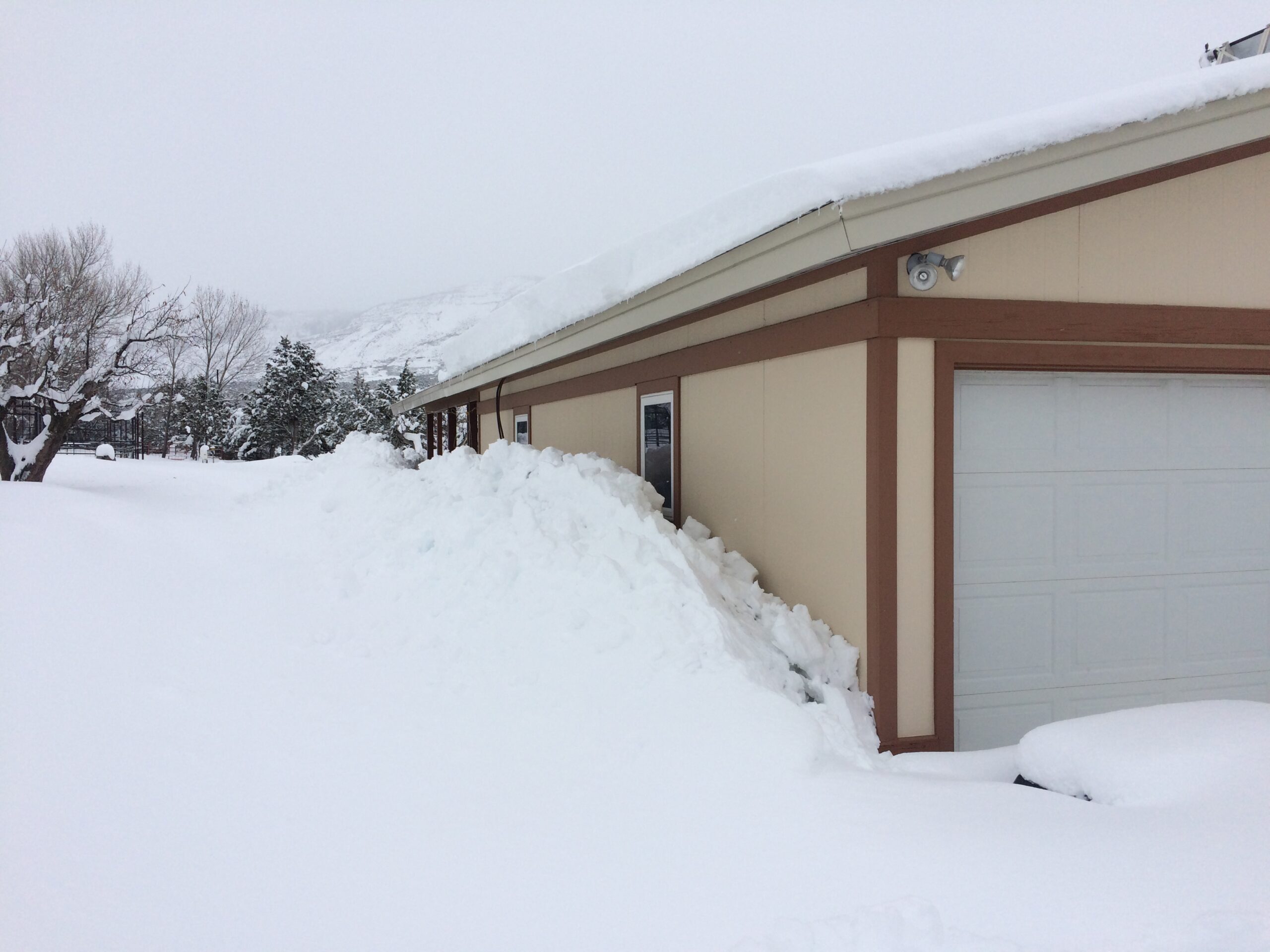 Large snow drifts collect against and obscure the walls of a garage. 