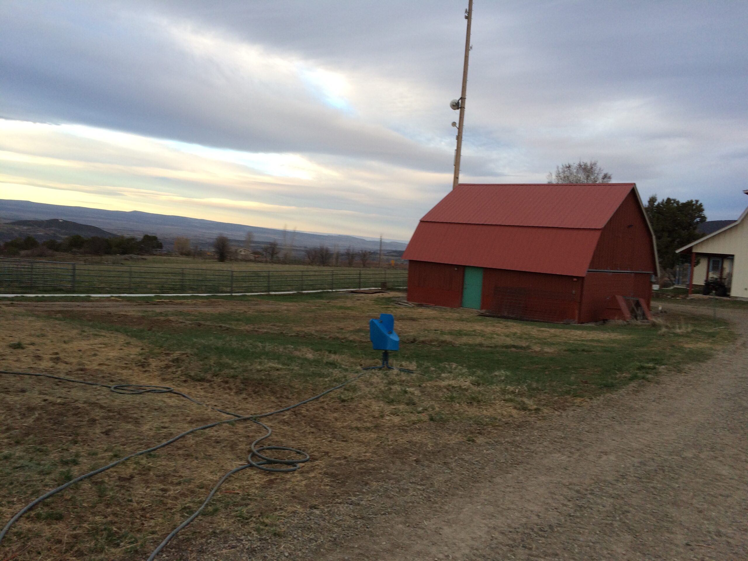An empty field with no corrals is in view next to a red barn. 
