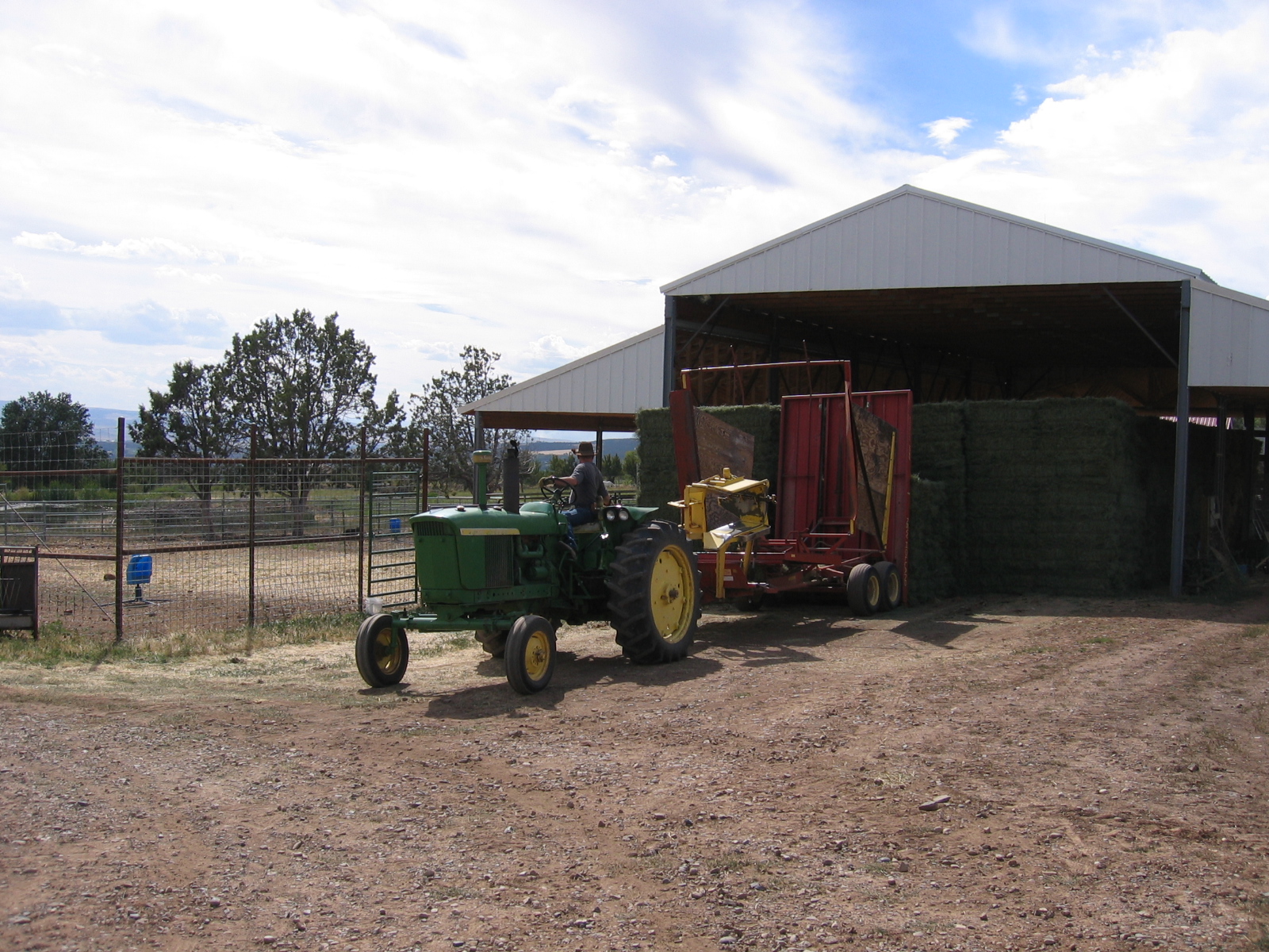 A tractor deposits fresh hay bales under the barn. 