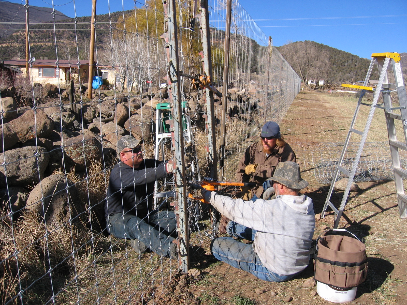 Workers are stretching the wire and attaching it to the fence posts behind it. 