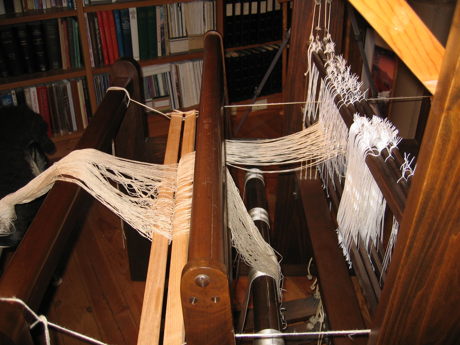 The loom is warped with various strings and threads for weaving. 