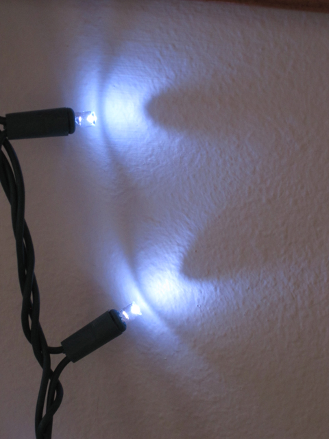 Two Christmas lights cast interesting shapes on a wall. 