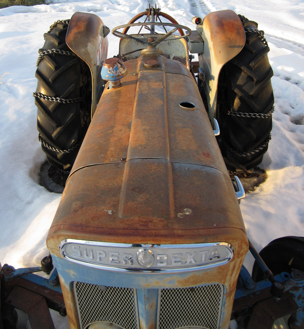 An old, rusty tractor sits in a patch of snow. 