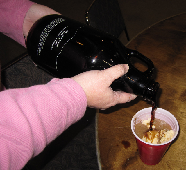 A root beer float is being poured into a red plastic cup.