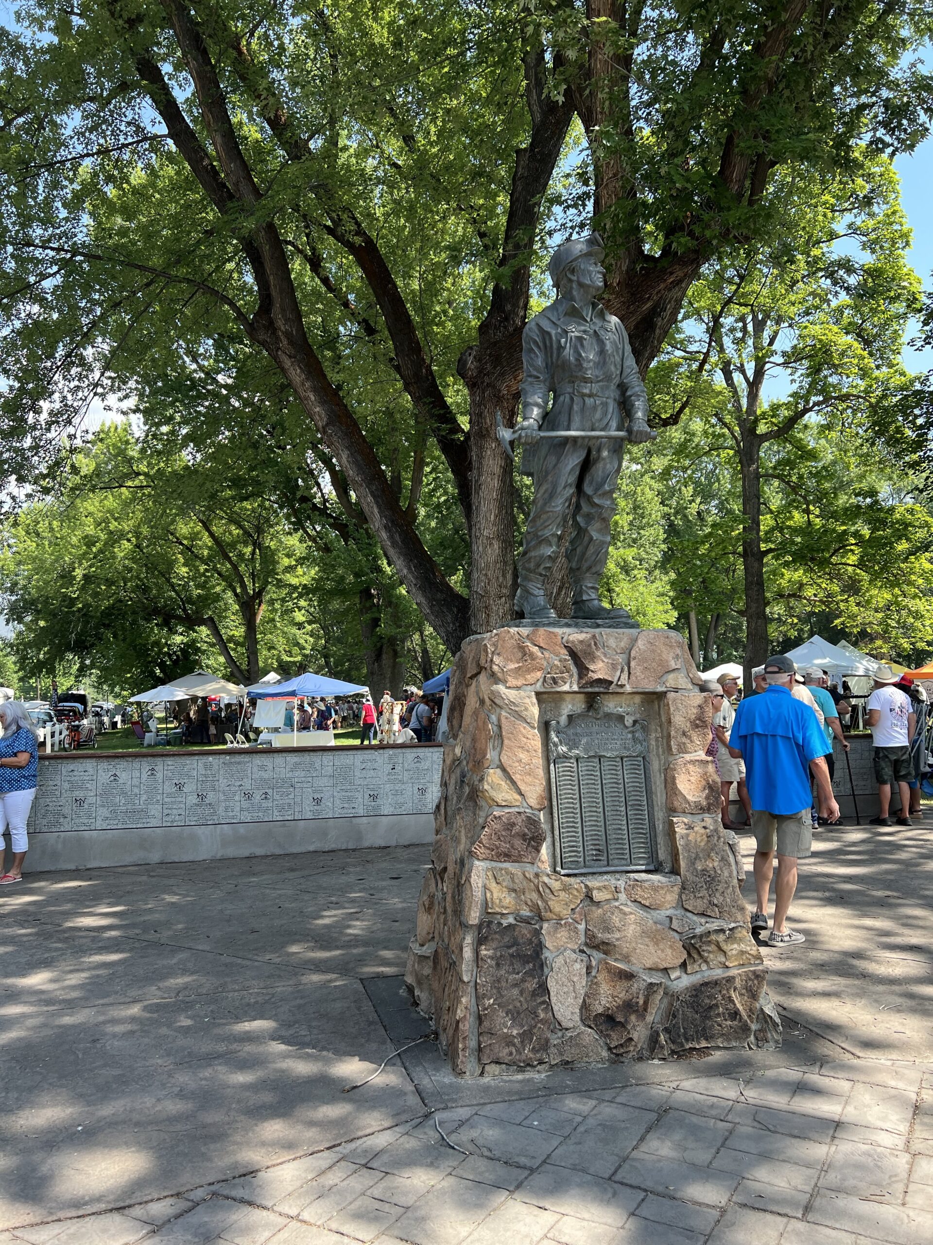 Booths and tents are set up in a park, with a memorial statue in the foreground. 